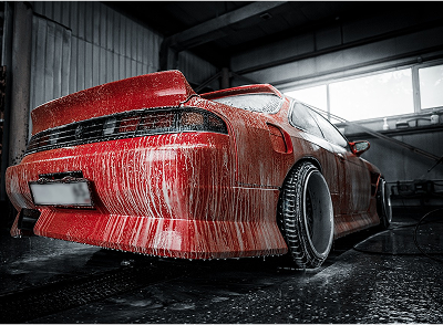 Red sports car covered in soap suds inside a garage.