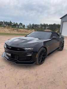 Sleek black sports car parked on a dirt driveway near a garage.