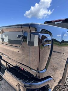 Close-up of a shiny black vehicle's side with reflections of the sky and surroundings.