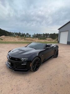 Black convertible sports car parked on a dirt road near a building.
