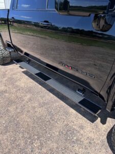 Close-up of a black vehicle's side step and reflective door surface.