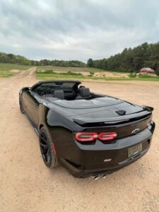 A sleek black convertible sports car parked on a dirt road under a cloudy sky.