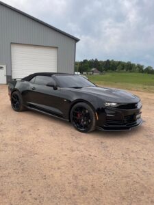 Sleek black sports car parked on a dirt surface near a garage.