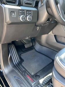 Driver's side footwell with pedals and floor mat in a vehicle.