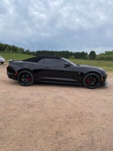 Black sports car parked on a gravel road with a green field background.