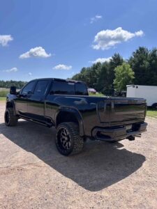 Black pickup truck parked on a sunny day with trees in the background.