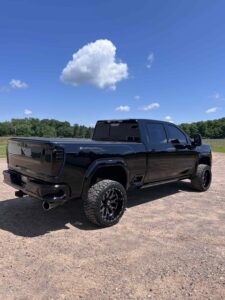 Black lifted pickup truck parked on a sunny gravel lot.