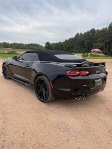 Black convertible sports car parked on a dirt road with trees in the background.