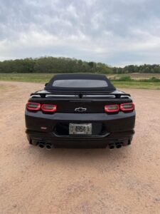 Rear view of a black Chevrolet Camaro on a dirt road.