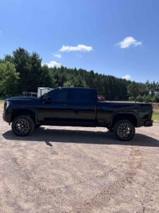 Black pickup truck parked on a gravel road with trees in the background.