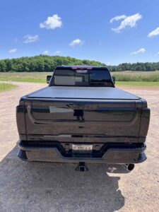 Black pickup truck parked on a rural road with fields and trees in the background.