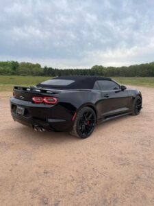 Sleek black sports car parked on a dirt road with a green landscape backdrop.