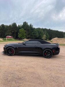 Black sports car parked on a dirt road near trees.
