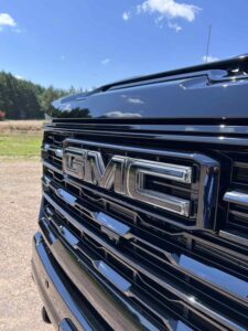 Close-up of a shiny black GMC truck grille under sunlight.
